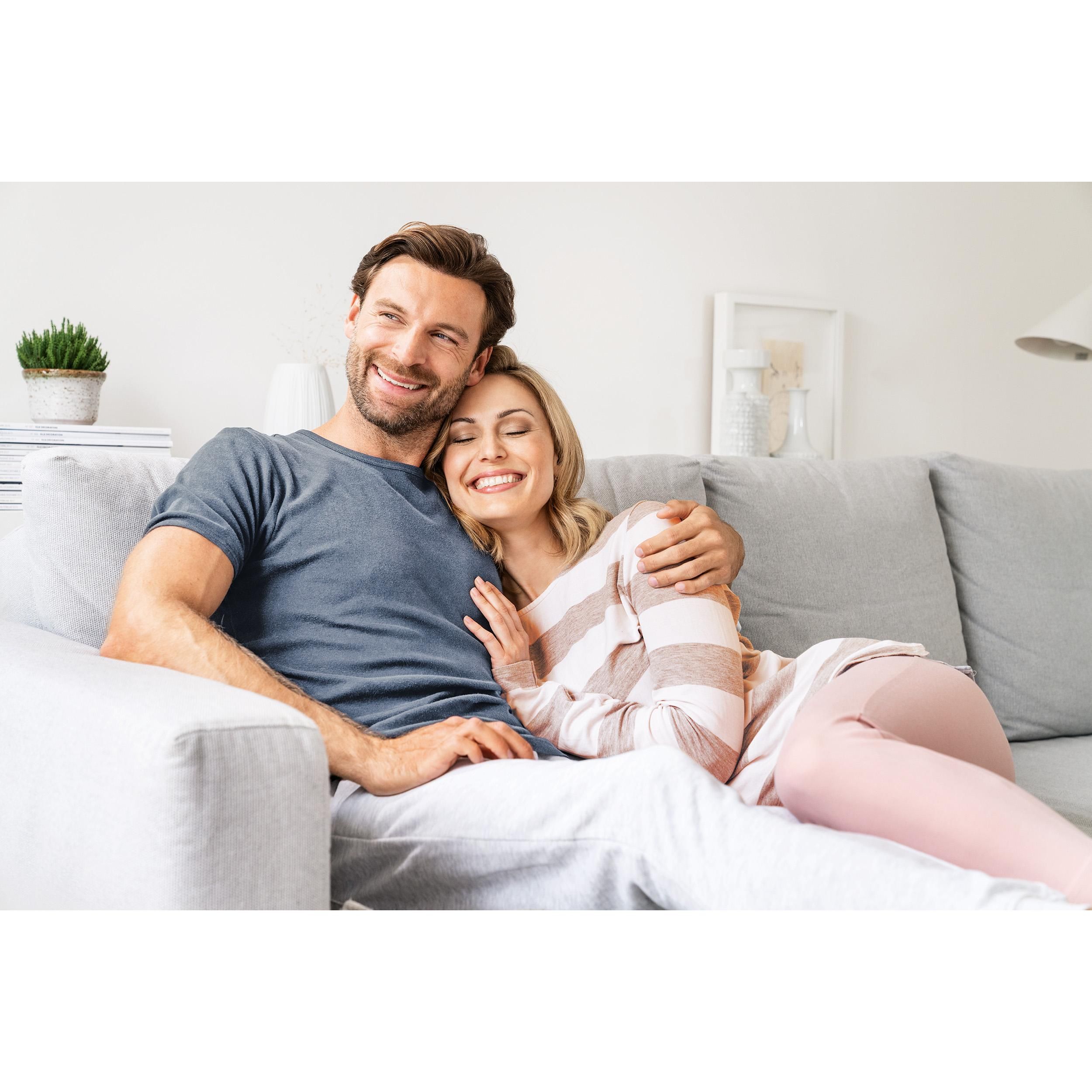 Ein Paar sitzt auf einem Sofa. Mann und Frau lächeln. Helle Umgebung.