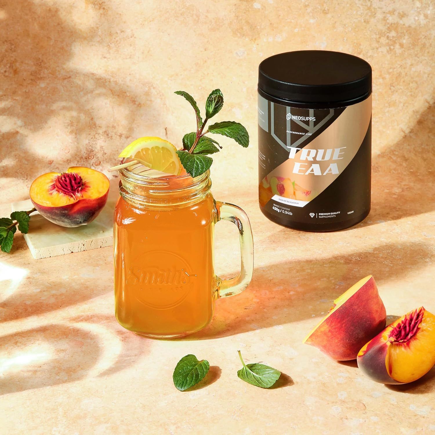 Schwarze Dose "TRUE EAA" neben Glas mit Getränk, Pfirsich und Minze. Dose mit Etikett. Text: 8 essentielle Aminosäuren + L-Histidin.