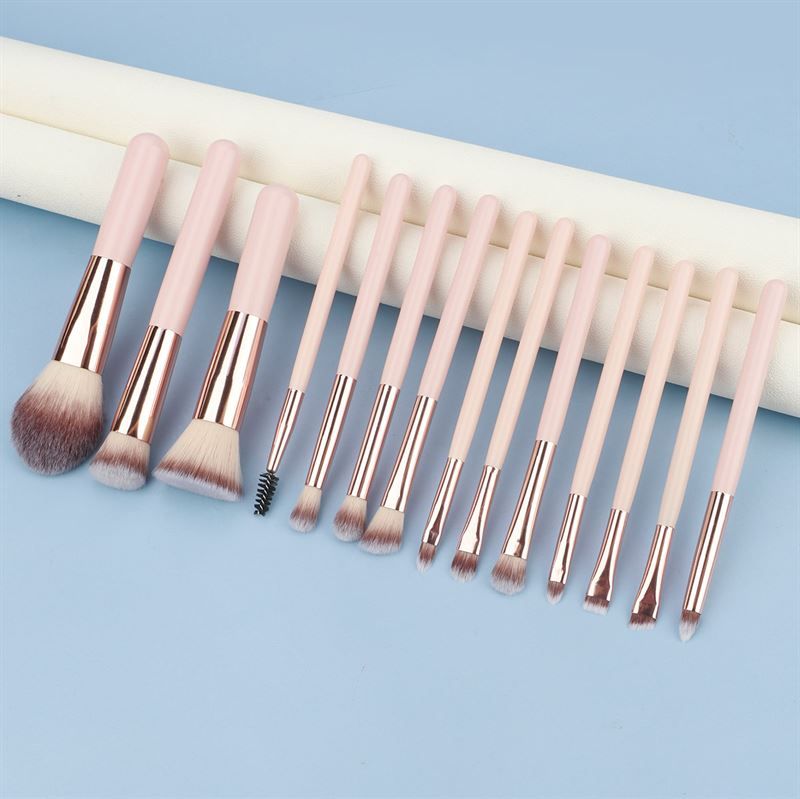 Make-up Pinsel-Set. Rosa Griffe, goldfarbene Metallhülsen, verschiedene Pinselköpfe. Auf blauem Untergrund.