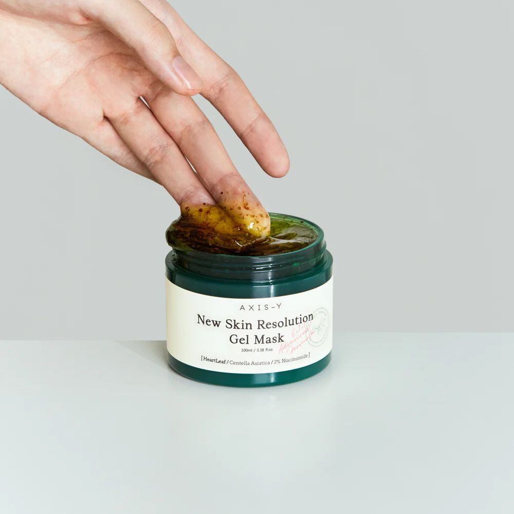 Ein Finger entnimmt Axis-Y New Skin Resolution Gel Maske aus einem Tiegel.