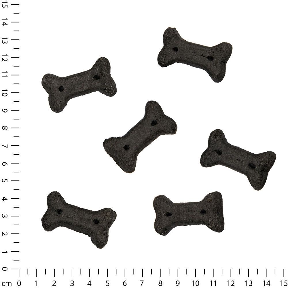 Sechs dunkle, knochenförmige Snacks mit Löchern, auf einem Lineal angeordnet.