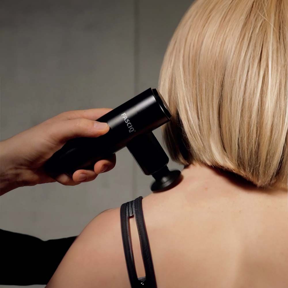 Schwarze Massagepistole an Schulter. Aufschrift FASCIQ. Person erhält Massage.
