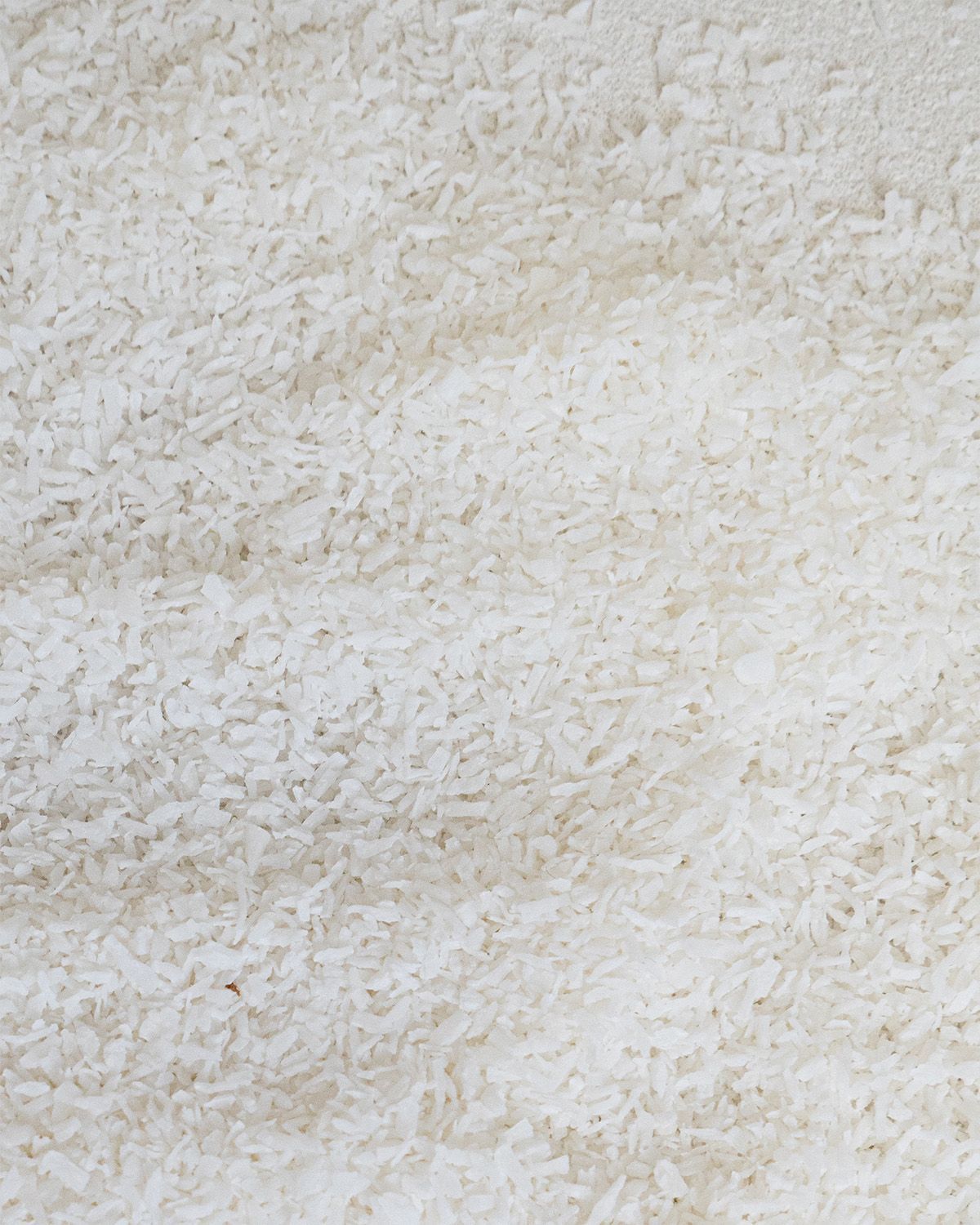 Nahaufnahme von weißen Kokosraspeln. Textur von vielen kleinen, unregelmäßigen Stücken.