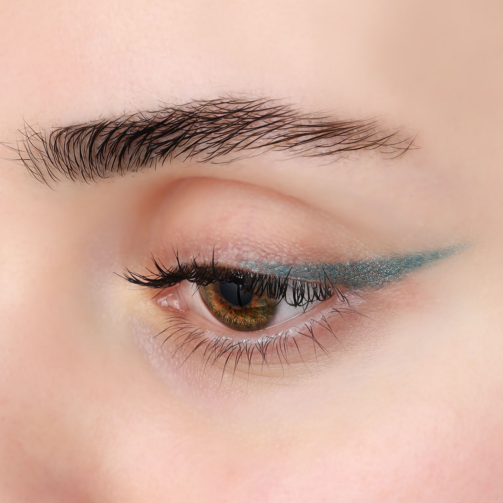 Nahaufnahme eines Auges mit türkisfarbenem Kajal-Eyeliner. Der Eyeliner ist am oberen Wimpernkranz aufgetragen.