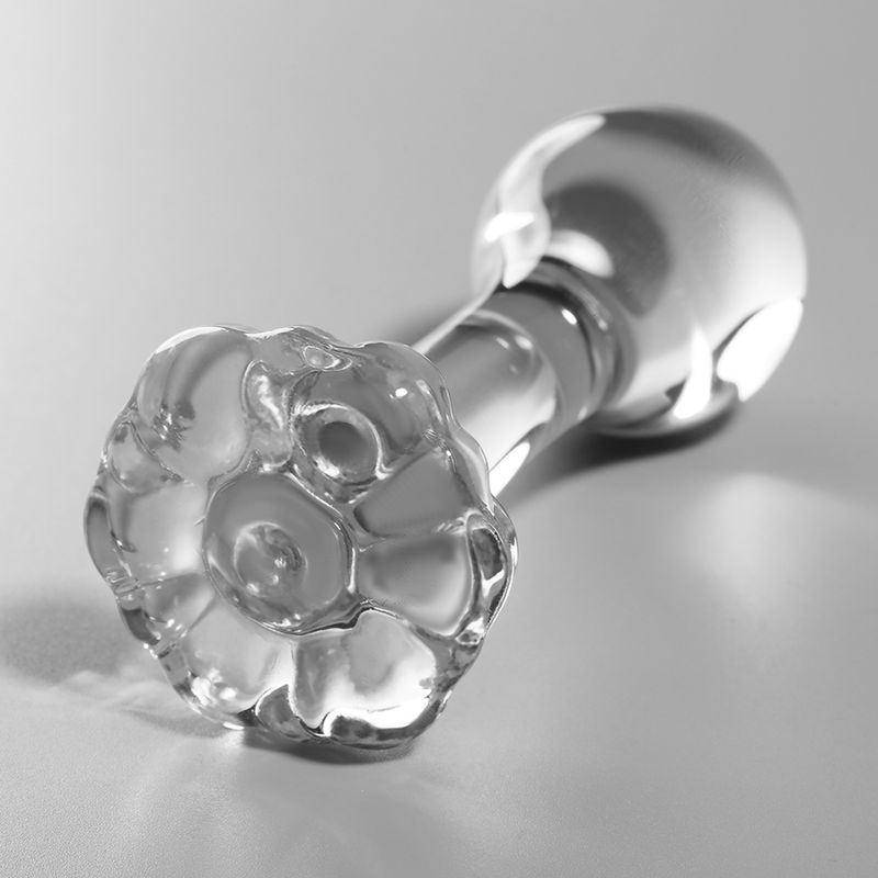 Klarer Glas-Analplug, liegend, mit detaillierter, blütenartiger Basis.