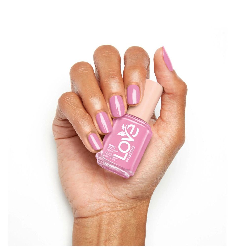 Hand mit lackierten Nägeln und Nagellackflasche. Rosa Nagellack von Essie.