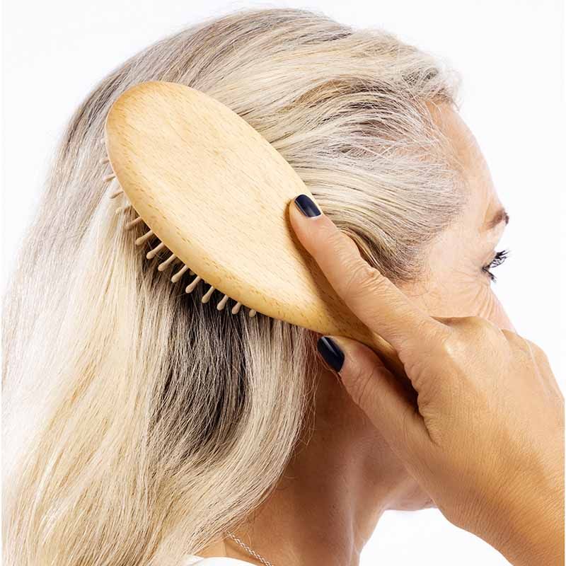 Eine Frau kämmt sich mit einer ovalen Holzbürste die Haare. Die Bürste hat helle Holzstifte. Die Frau hat graue Haare.