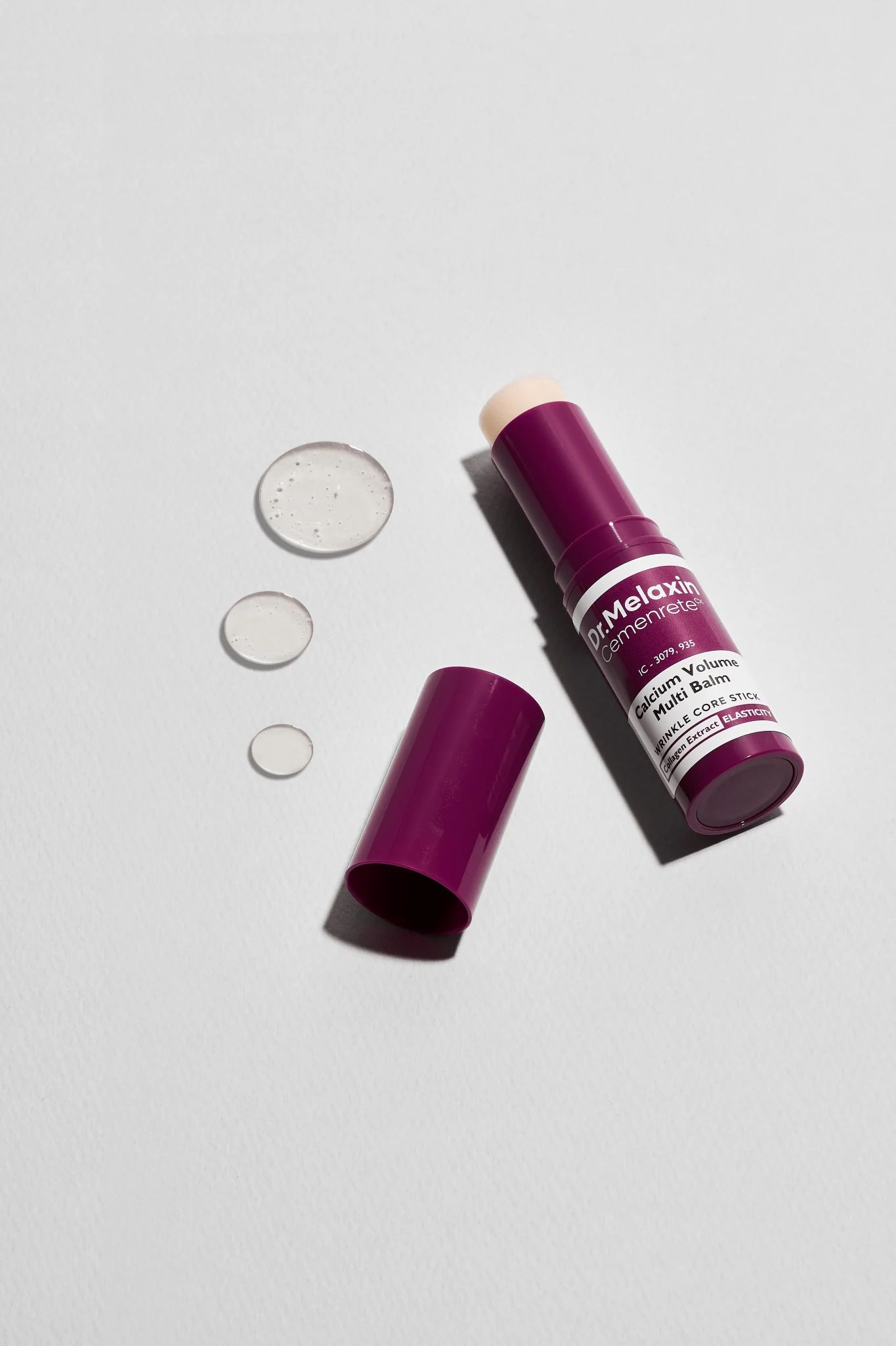 Dr.Melaxin Cemenrete Calcium Volume Multi Balm. Produkt mit geöffneter Kappe und Tropfen. Lila Verpackung.