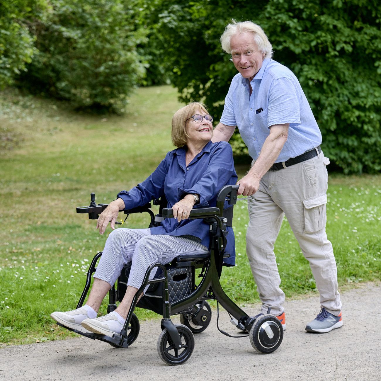 Mann schiebt Frau in einem elektrischen Rollator im Park.
