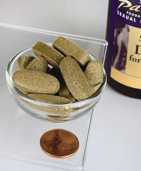 Braune Tabletten in einer Glasschale. Daneben eine Münze und eine Flasche mit Etikett.