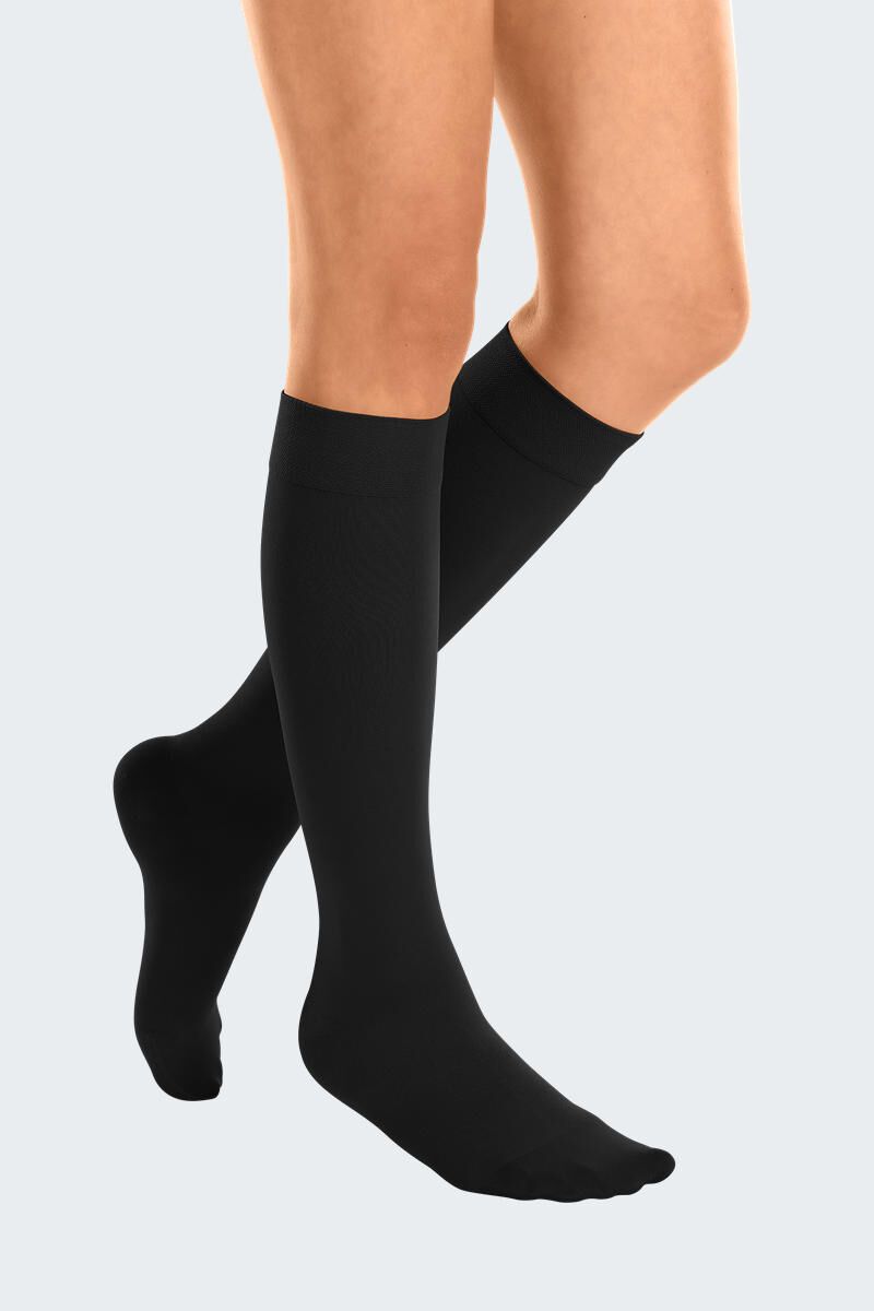 Schwarze Kompressionsstrümpfe, knielang, an Beinen einer Person. Feines, geripptes Muster. Blick von der Seite.