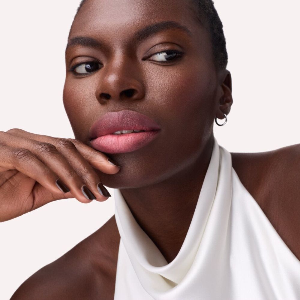 Porträt einer Frau mit rosafarbenem Lippenstift. Sie trägt ein weißes Oberteil und Ohrringe.