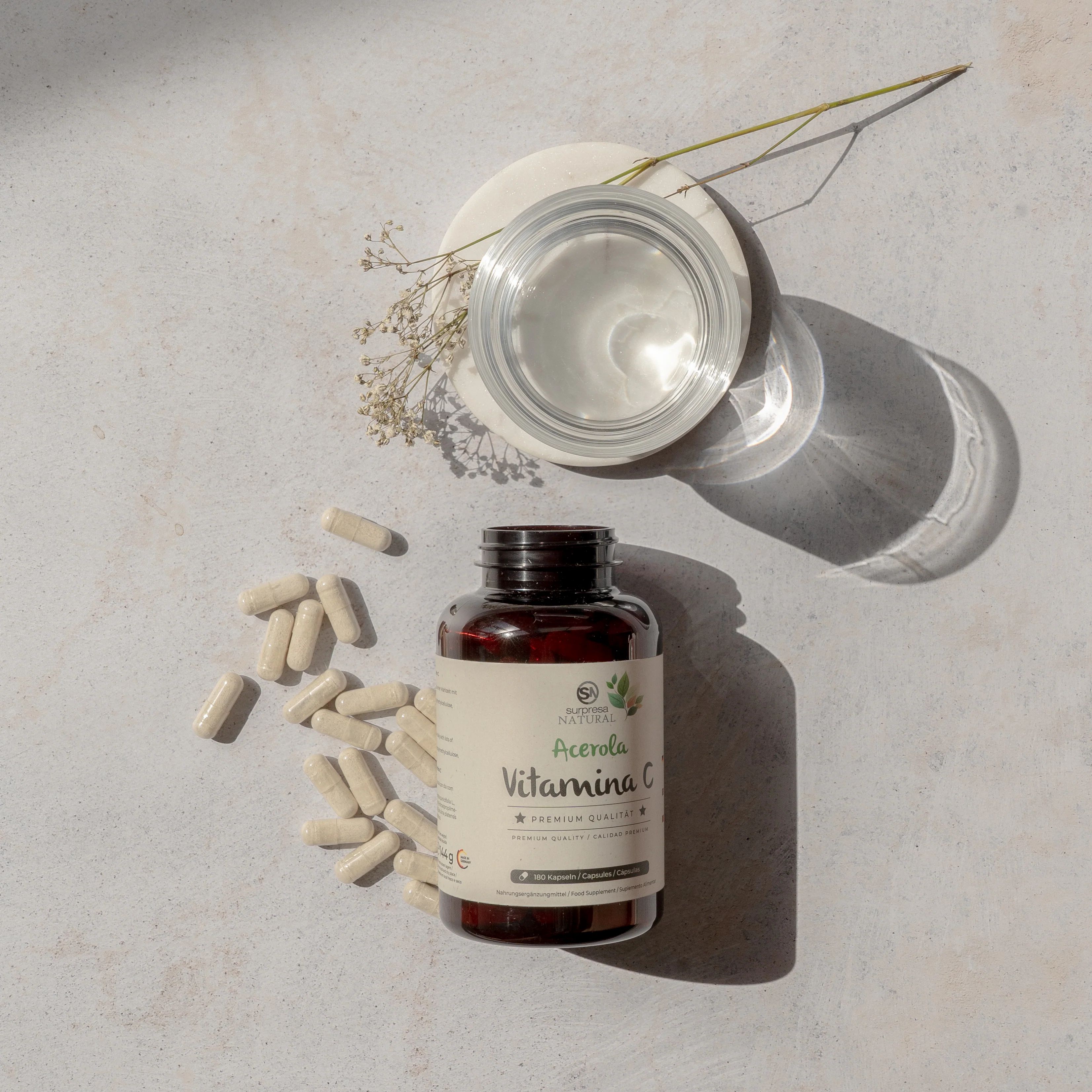 Braune Flasche mit Kapseln und Glas auf hellem Untergrund. Aufschrift: Acerola Vitamin C. Premium Qualität.