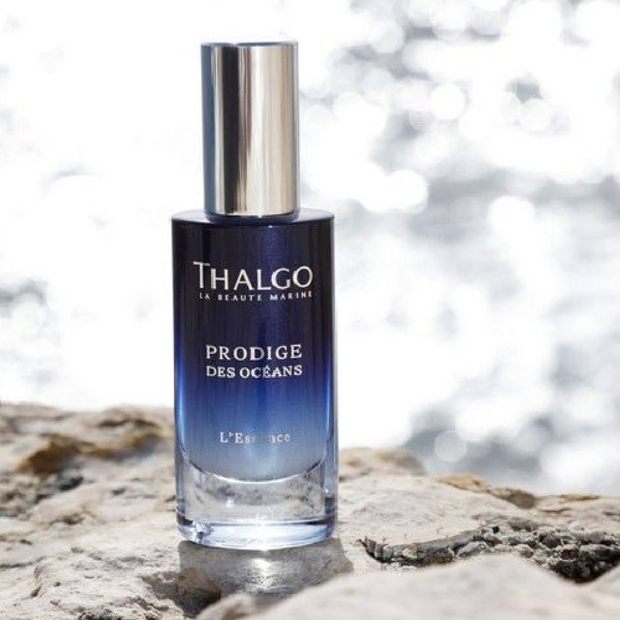 Glasflasche mit blauem Farbverlauf und silbernem Deckel. Beschriftung: THALGO, PRODIGE DES OCEANS, L'Essence. Auf Stein platziert.