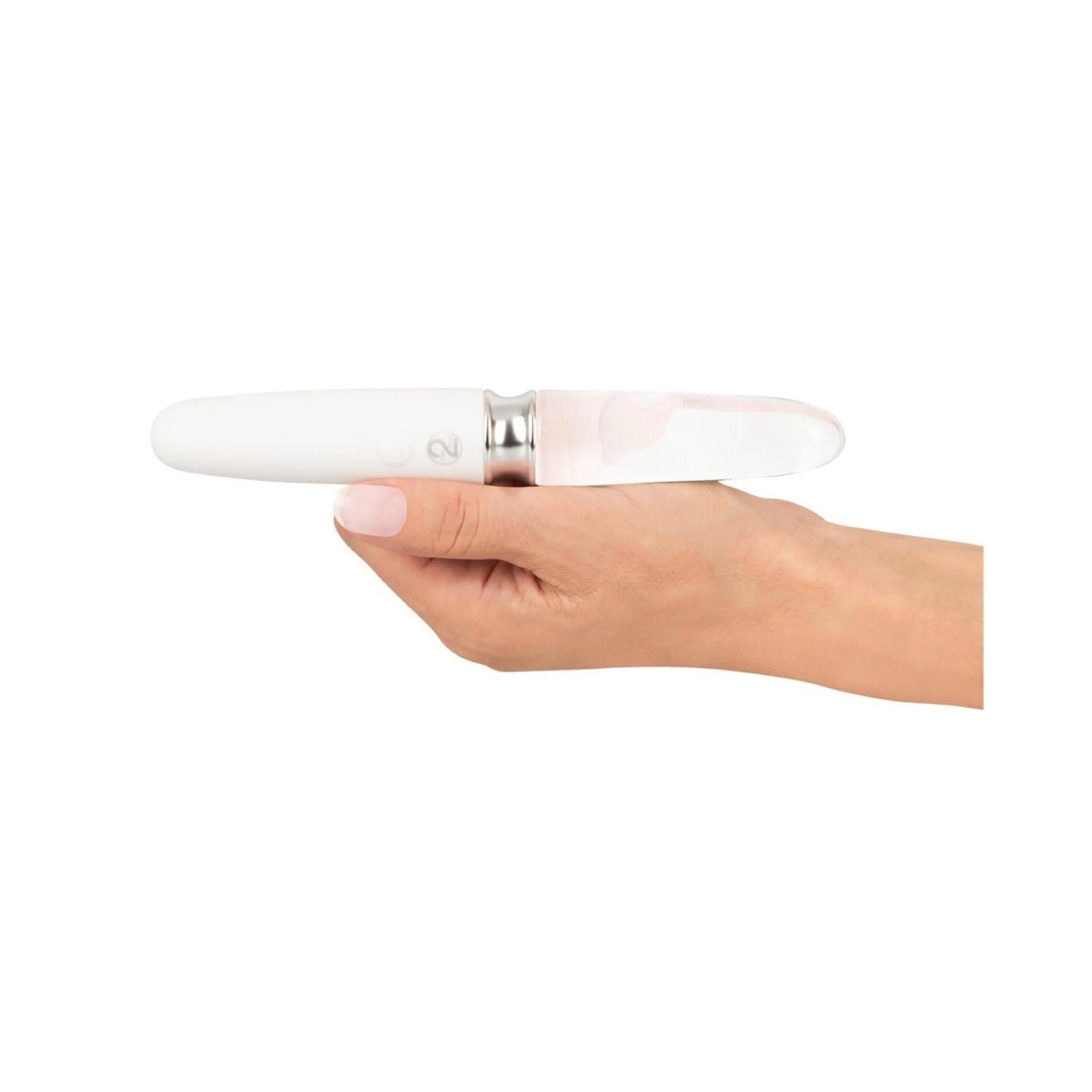 Weißer, länglicher Vibrator mit transparentem, konischem Ende. Silberfarbener Ring in der Mitte. Ein/Aus-Taste. Gehalten von einer Hand.