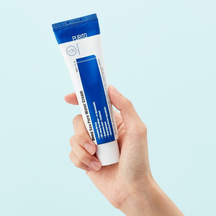 Hand hält eine Tube. Auf der Tube steht Deep Sea Pure Water Cream. Die Tube ist weiß und blau. Der Hintergrund ist hellblau.