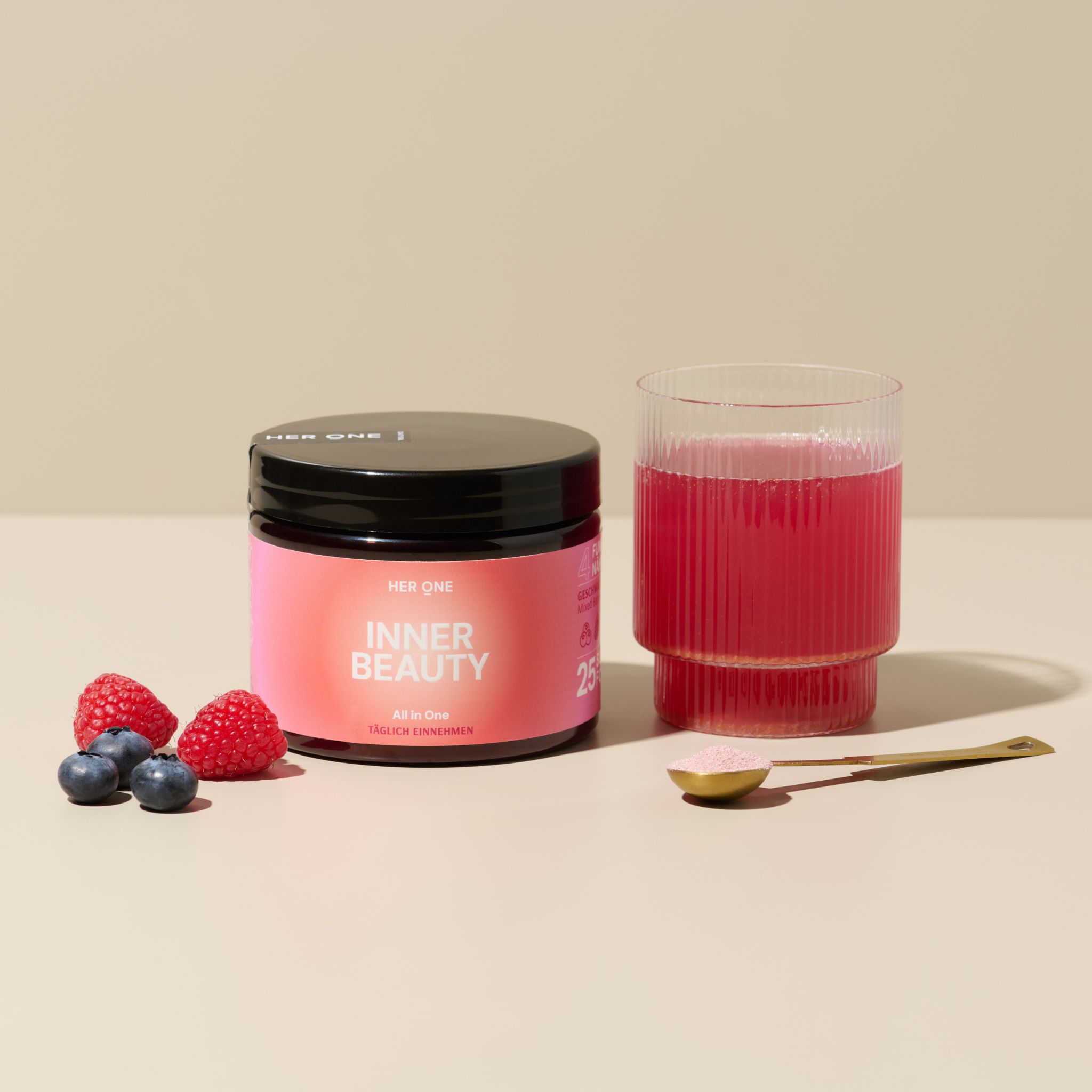 Produkt und Glas mit Getränk. Beeren und Löffel daneben. Aufschrift: HER ONE INNER BEAUTY ALL IN ONE.
