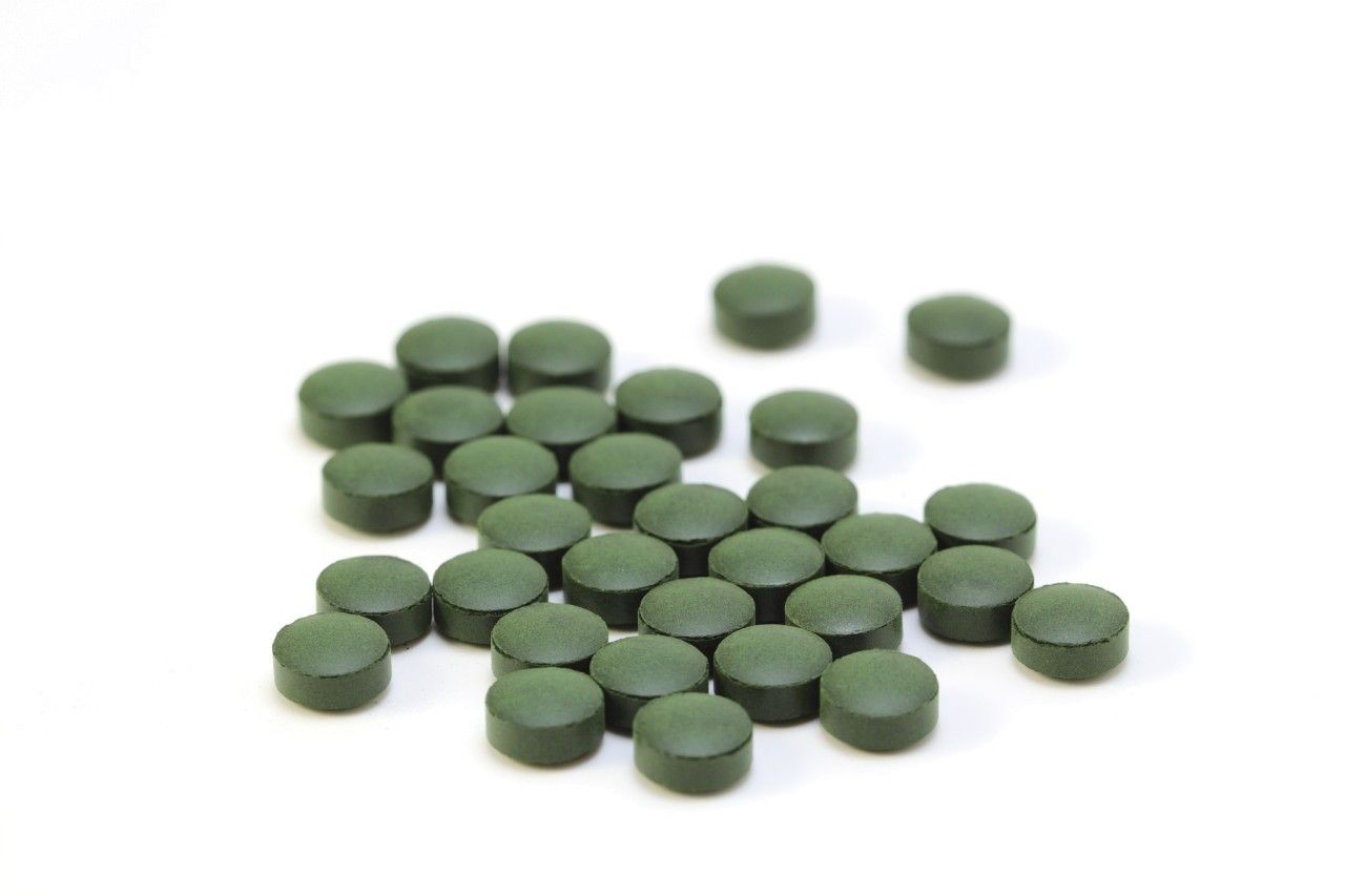 Haufen grüner, runder Tabletten auf weißem Hintergrund. Tabletten sind flach und haben eine runde Form.