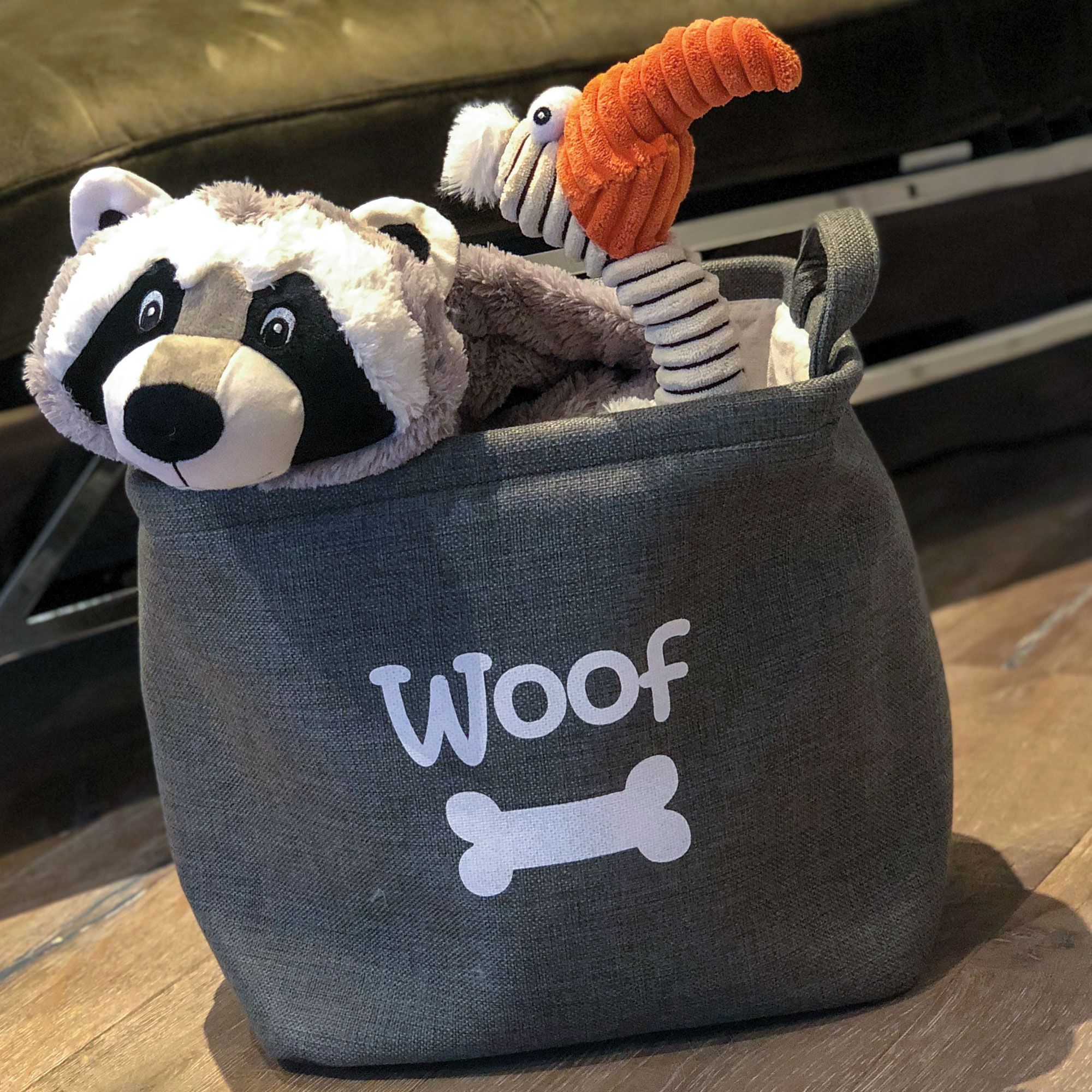Graue Stofftasche mit Aufdruck 'Woof' und Knochen. Enthält ein Waschbär- und ein Geier-Plüschtier.