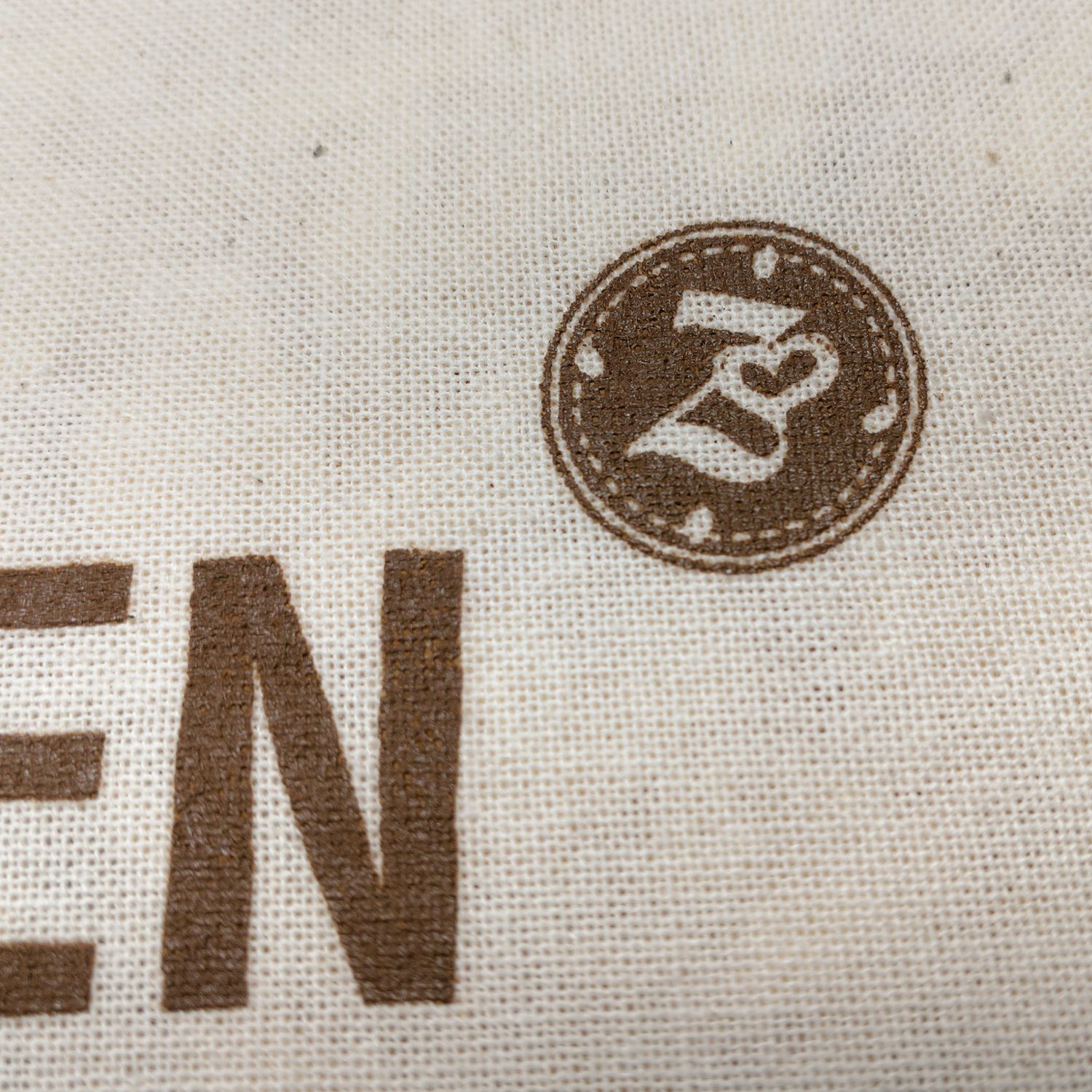 Nahaufnahme des Logos auf einem Kissen. Logo: brauner Kreis mit Herz und Schriftzug.