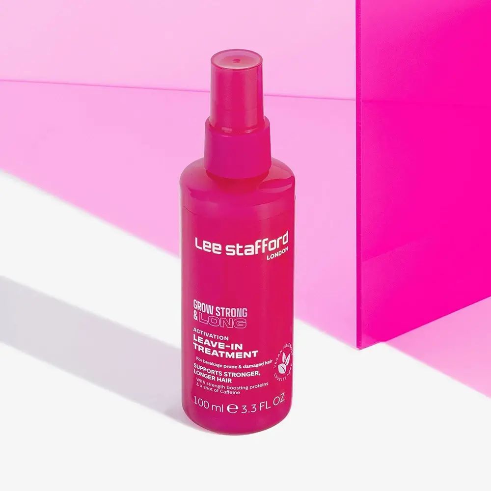 Rosa Sprühflasche. Beschriftung: Grow Strong & Long Leave-In Treatment. Marke: Lee Stafford. Vegan-Logo. Rosa Hintergrund.