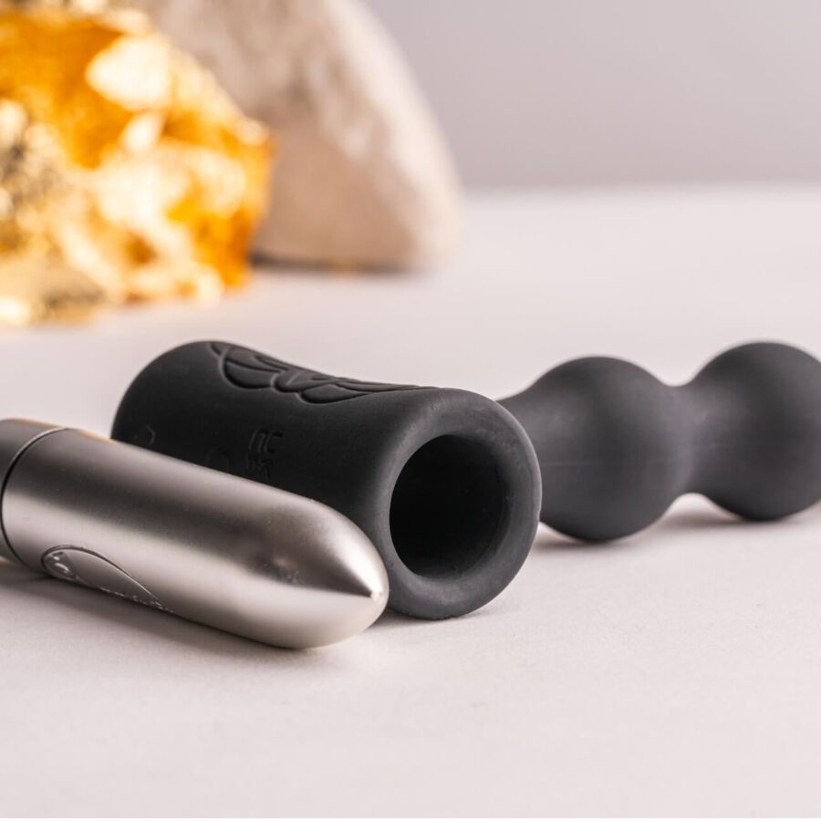 Drei Teile: ein metallisches, zylindrisches Element, ein schwarzer Ring und ein geriffelter Plug.