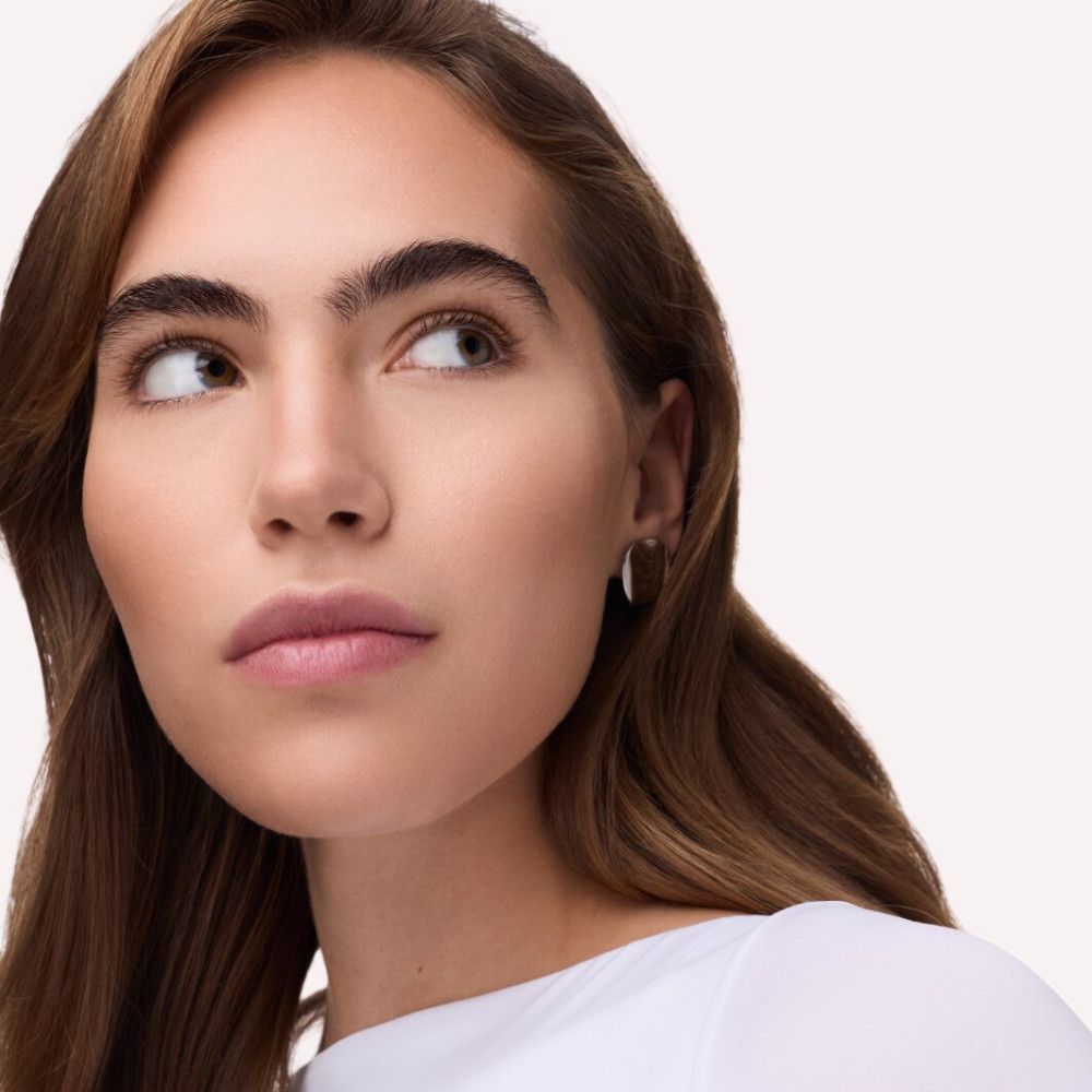 Porträt einer Frau mit hellem Teint. Sie trägt einen weißen Pullover und schaut zur Seite.