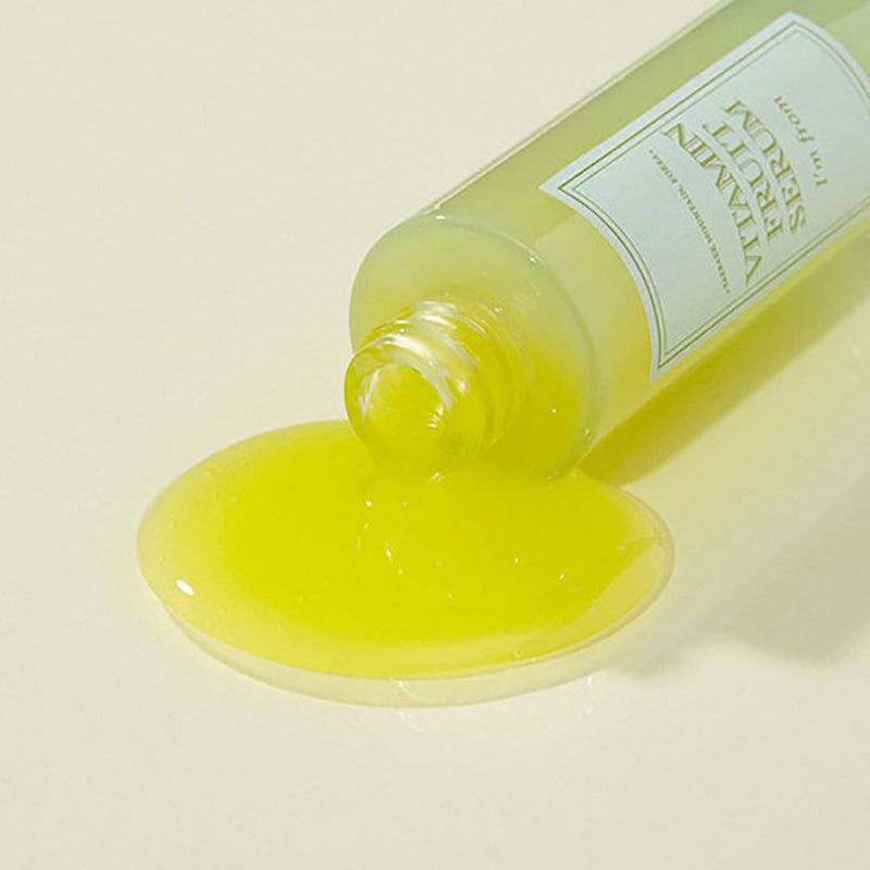 Serum fließt aus einer Flasche. Gelbe Flüssigkeit bildet eine Pfütze. Flasche mit Aufschrift: Vitamin Fruit Serum.