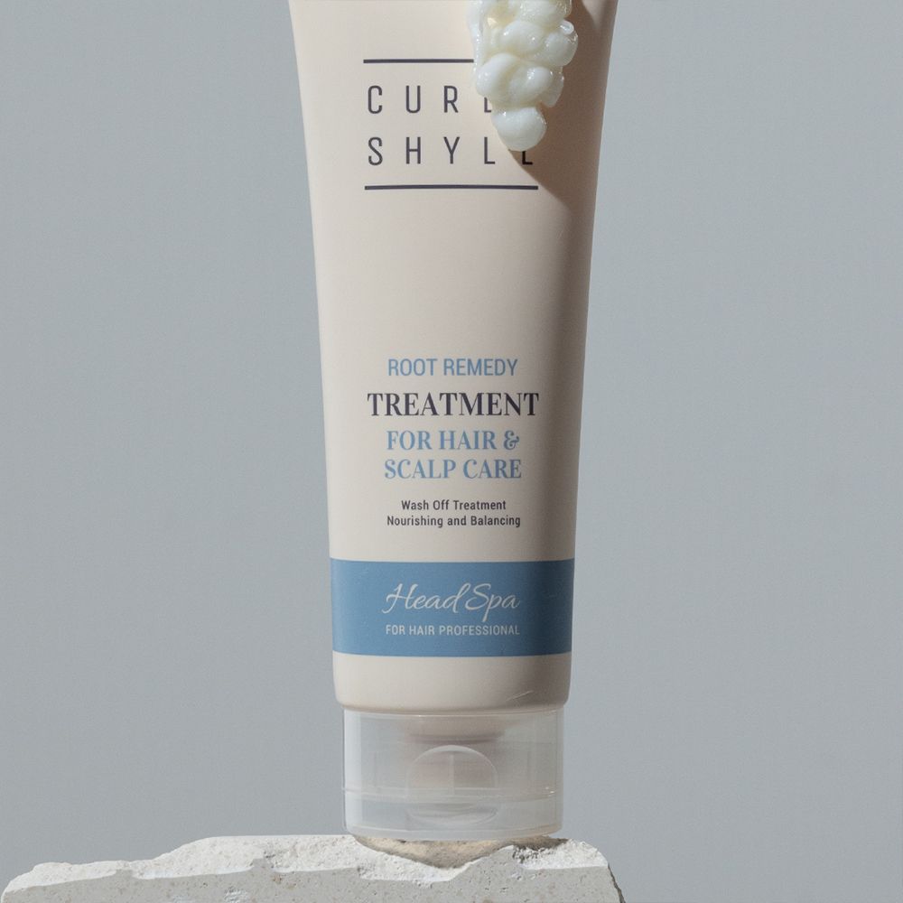 Beige Tube mit Schriftzug CURLY SHYLL, Root Remedy Treatment für Haar & Kopfhautpflege. Blaue Leiste mit Head Spa. Auf Stein.