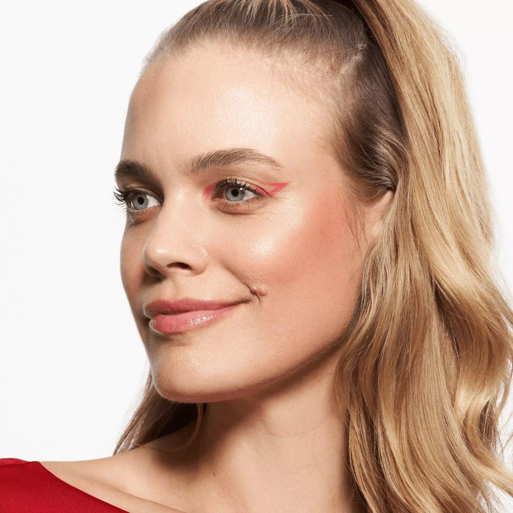 Porträt einer Frau mit blonden Haaren. Sie trägt rosafarbenen Lippenbalsam und roten Eyeliner.