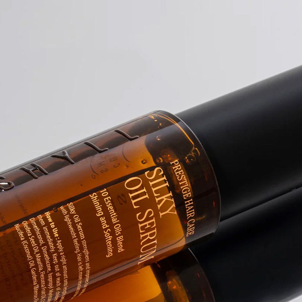 Nahaufnahme einer braunen Haarölflasche mit schwarzem Deckel. Aufschrift: Silky Oil Serum. Für professionelle Haarpflege.