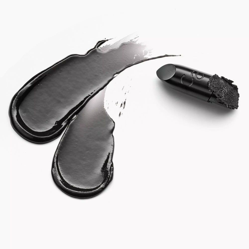 Schwarze Lippenstift-Textur auf weißem Hintergrund. Daneben liegt ein Lippenstift. Marke: Catrice.