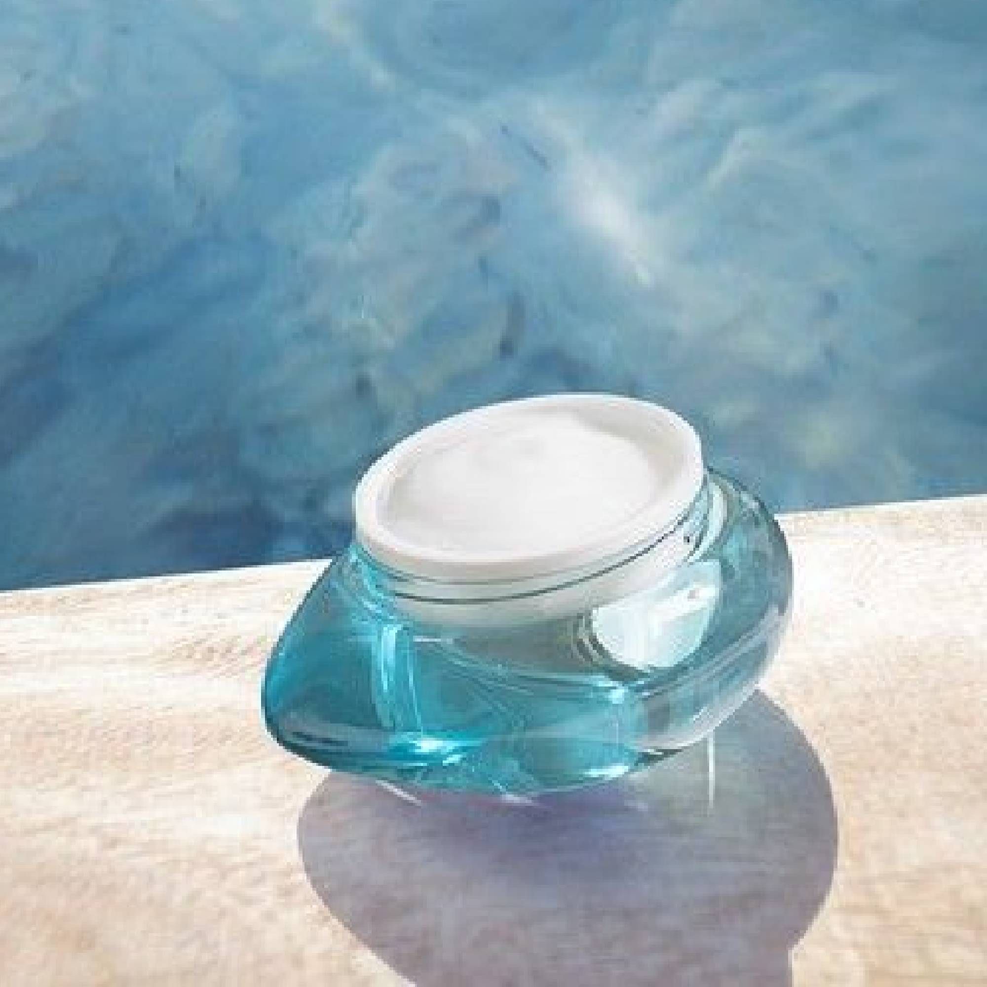 Türkisfarbener Cremetiegel mit weißem Deckel, auf einer Holzoberfläche. Spiegelung.