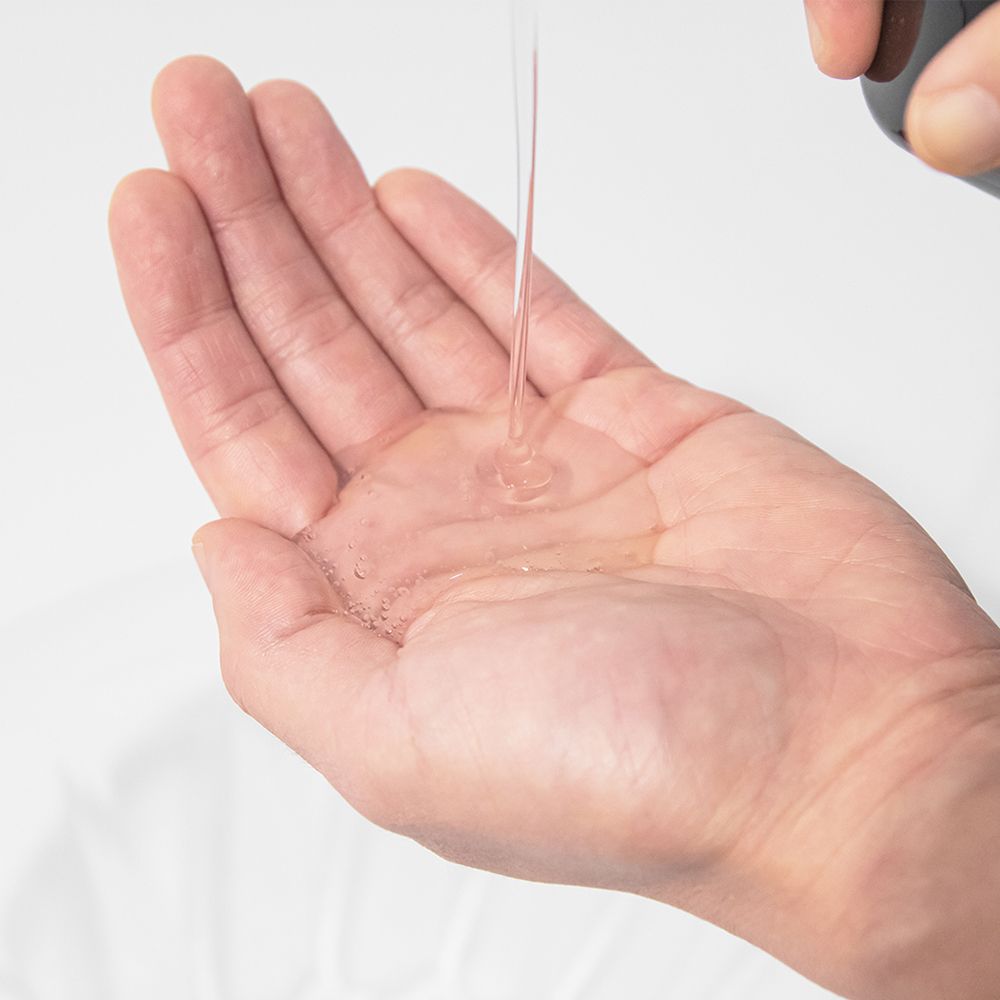 Hand, die eine transparente Flüssigkeit empfängt. Flüssigkeit wird aus einer Flasche gegossen.