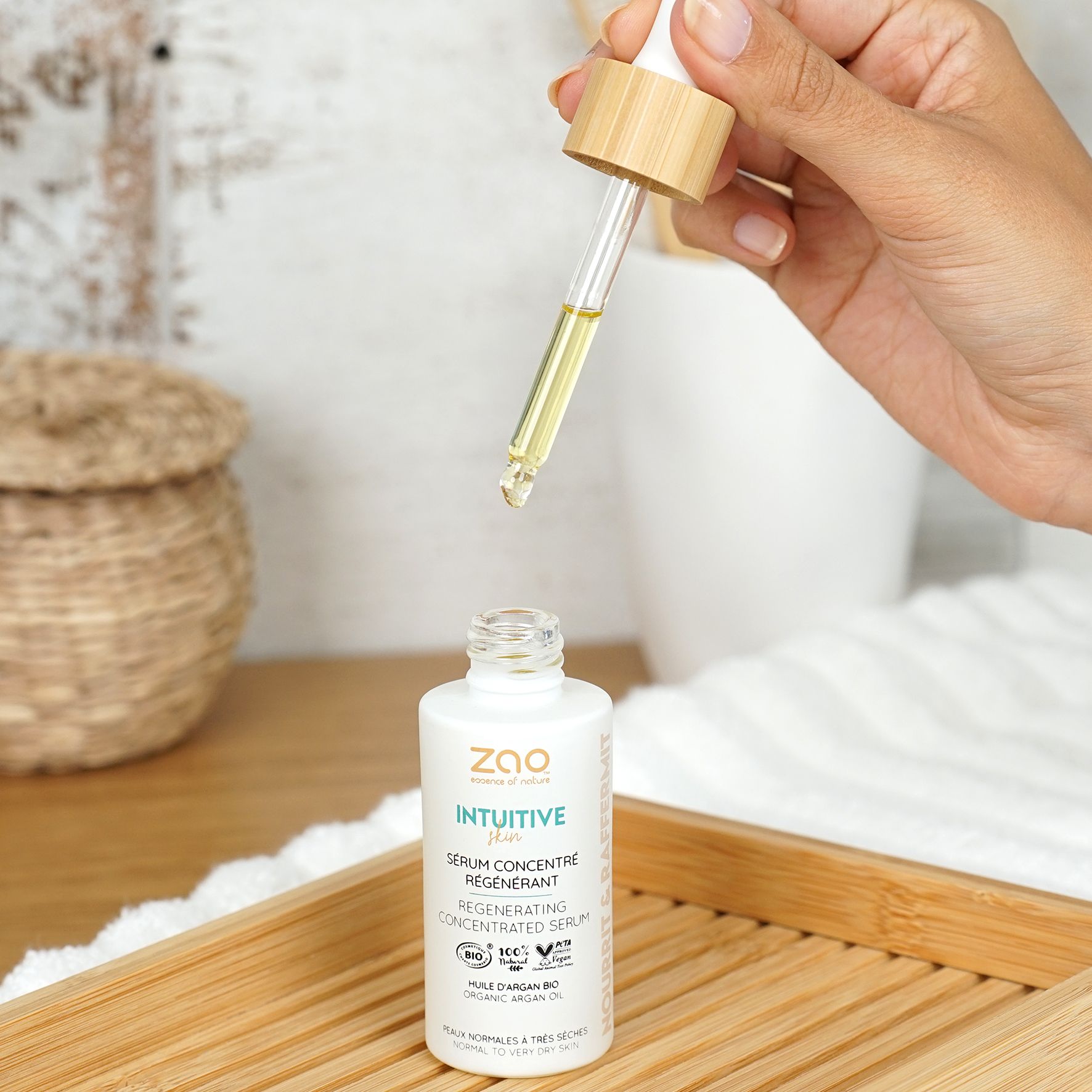 Weißes Fläschchen mit Pipette. Tropfen Serum. Aufschrift: ZAO, Intuitive, Serum concentré régénérant. Auf Holztablett.