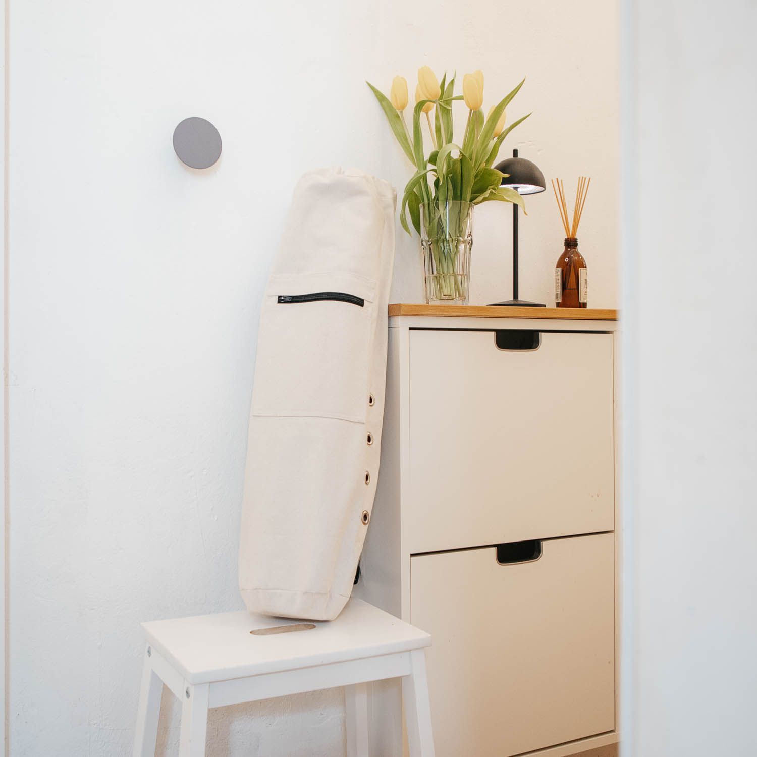 Beige Yogamatten Tasche an einem Hocker. Reißverschluss, Knöpfe und schwarze Details.