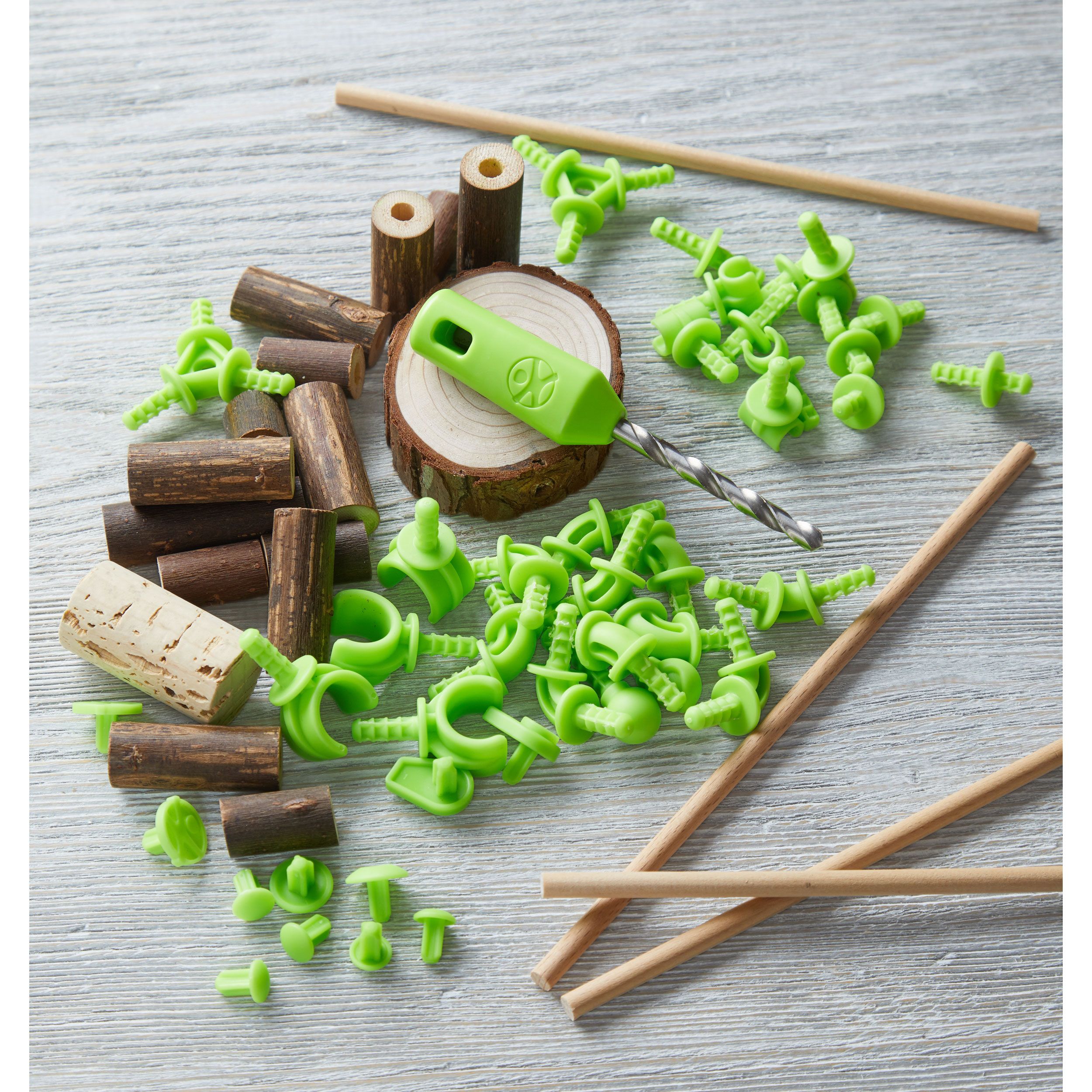 Konstruktions-Set mit Holzstücken, grünen Verbindern, Kork, Holzscheibe und Werkzeug. Einzelteile liegen auf einer Holzoberfläche.