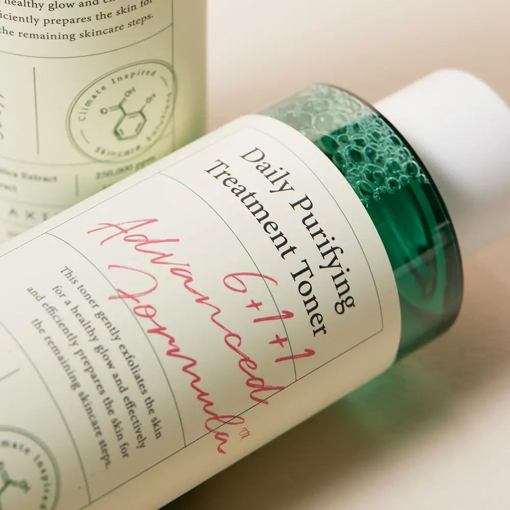 Nahaufnahme einer Tonerflasche. Aufschrift: Daily Purifying Treatment Toner. Grüne Flüssigkeit sichtbar.