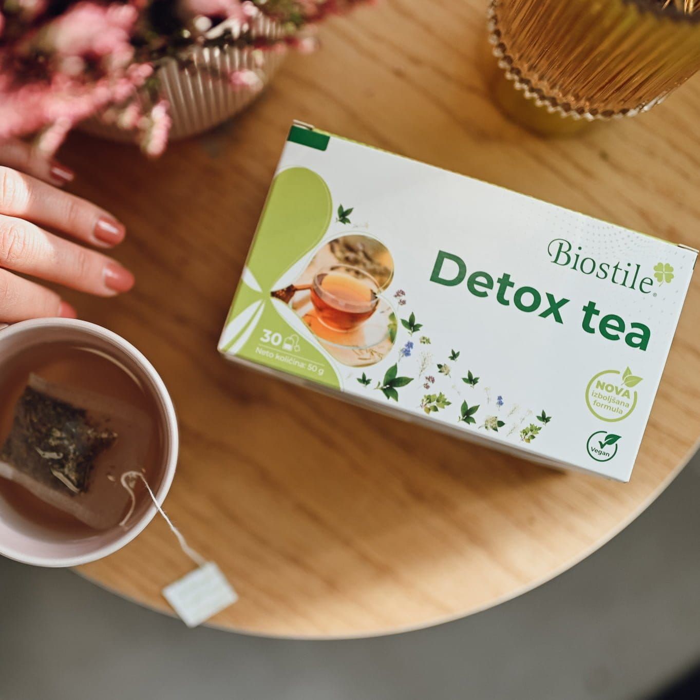 Eine Person hält eine Tasse Tee mit einem Teebeutel. Daneben eine Packung Biostile Detox Tea.