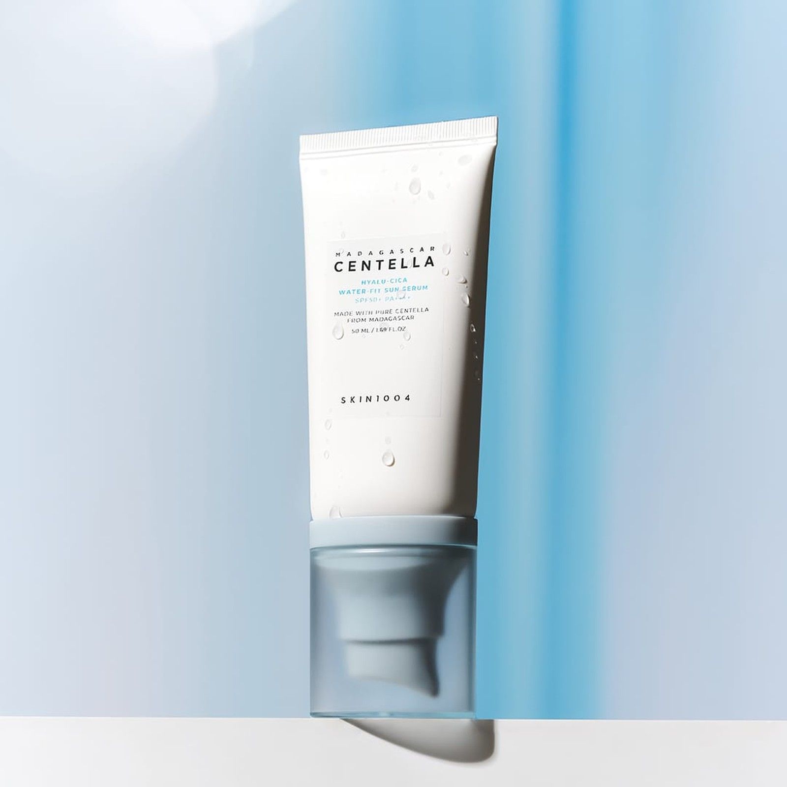 SKIN1004 Hyalu-Cica Water-Fit Sonnenserum SPF 50+ PA++++ mit Wassertropfen auf der Tube, vor blauem Hintergrund.
