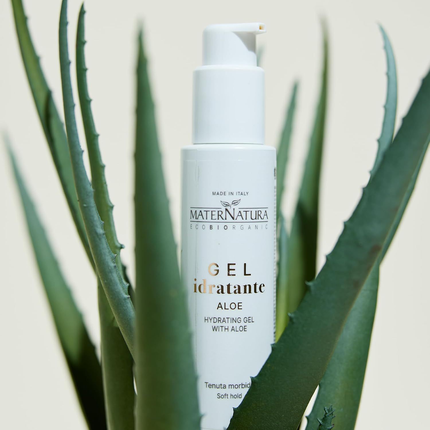 Weiße Flasche mit Pumpspender, umgeben von Aloe-Vera-Pflanzen. MATERNATURA, GEl idratante ALOE.