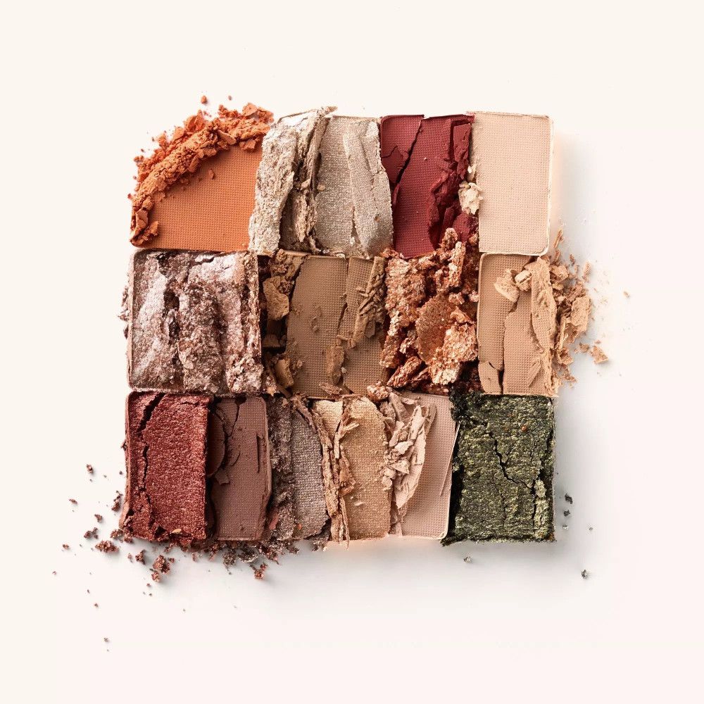 Quadratische Anordnung von 12 Lidschattenfarben. Farben: Orange, Gold, Rot, Beige, Braun, Grün. Einige Lidschatten sind zerbrochen.