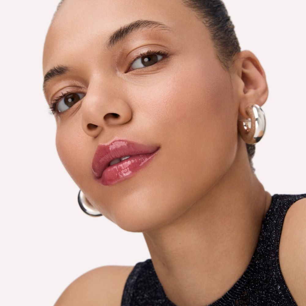 Porträt einer Frau mit glänzendem Lipgloss. Sie trägt silberne Creolen und ein schwarzes Top.