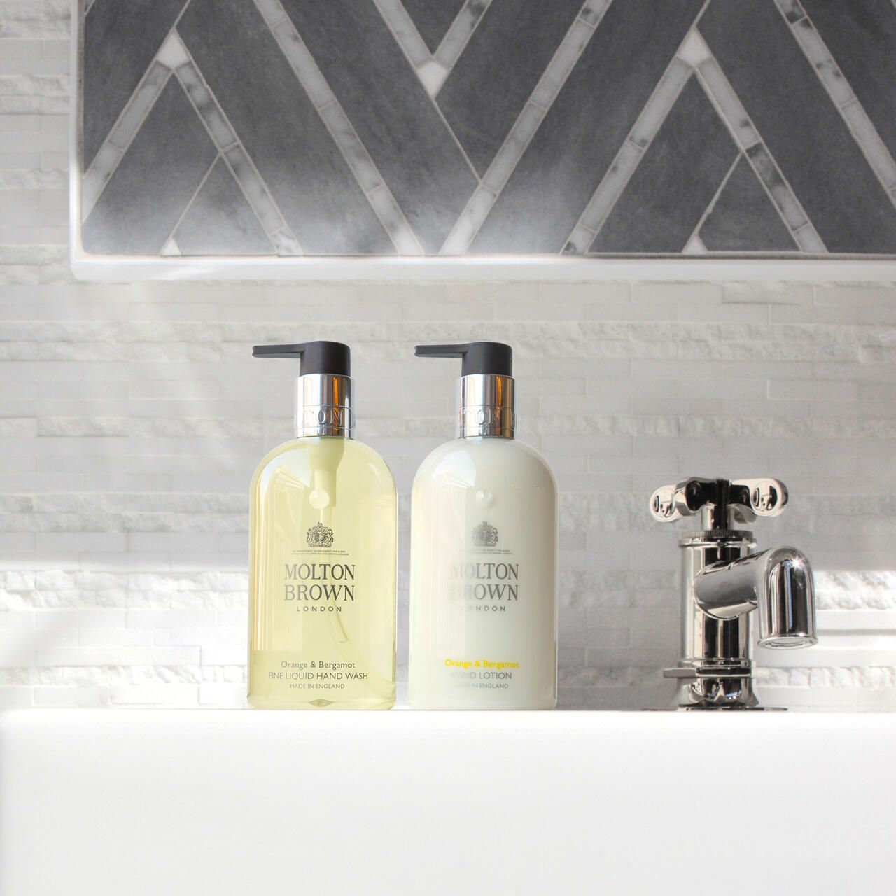 Zwei Flaschen Molton Brown Handseife am Waschbecken. Eine gelb, eine weiß. Wasserhahn daneben.