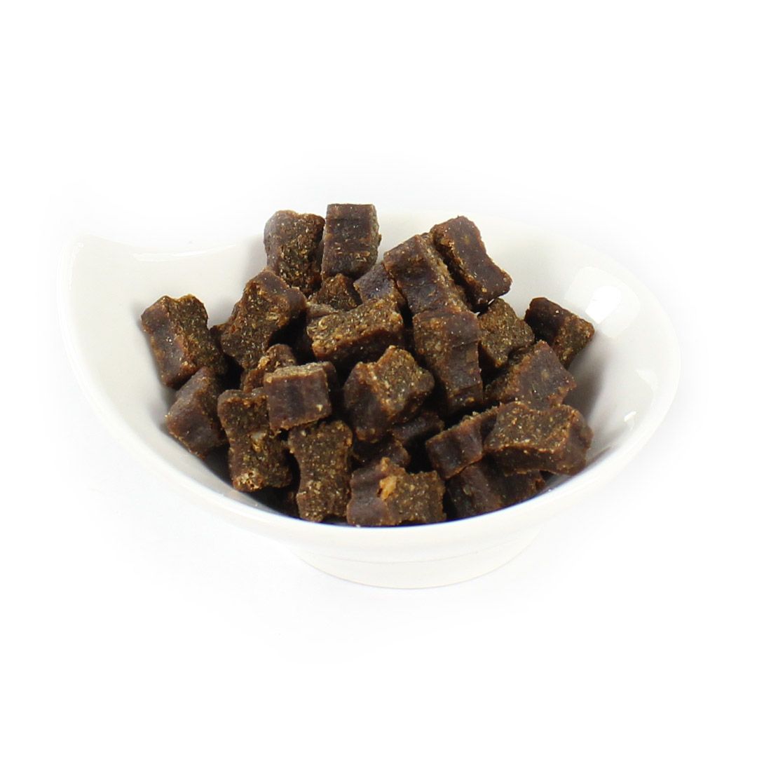 Hundefutter in einer weißen Schale. Kleine, braune, quadratische Stücke.