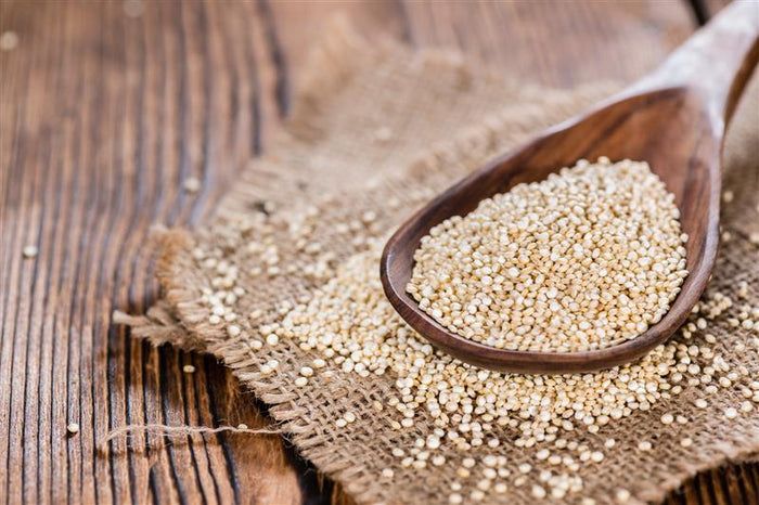 Holzlöffel mit Quinoa-Samen auf einem Leinentuch. Holzstruktur im Hintergrund.