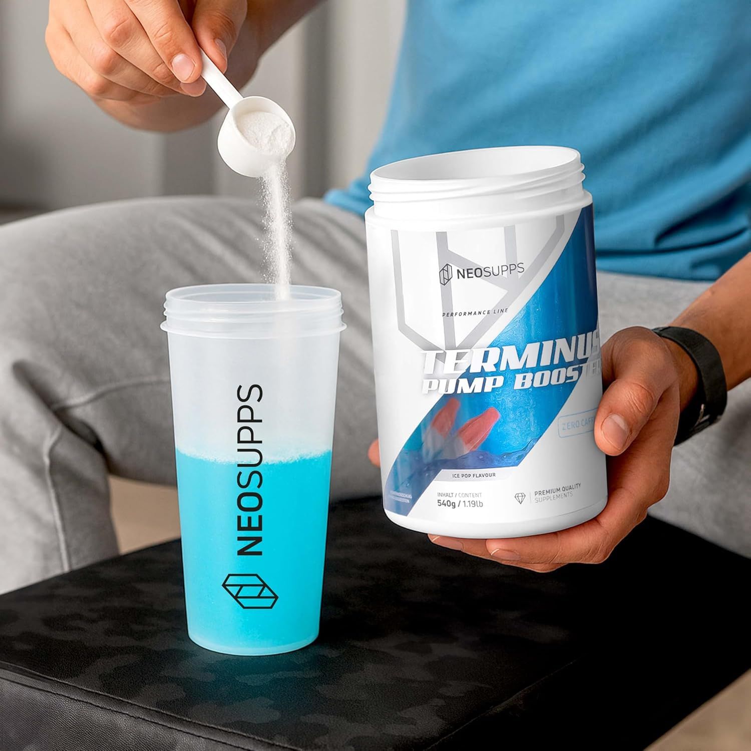 Person gießt Pulver aus Dose in Becher. Dose: TERMINUS PUMP BOOSTER, NEOSUPPS. Becher: NEOSUPPS. Blaue Flüssigkeit im Becher.