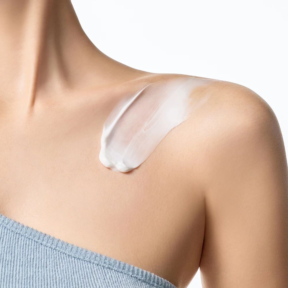 Helle Haut mit aufgetragener Creme auf der Schulter. Blauer Top.