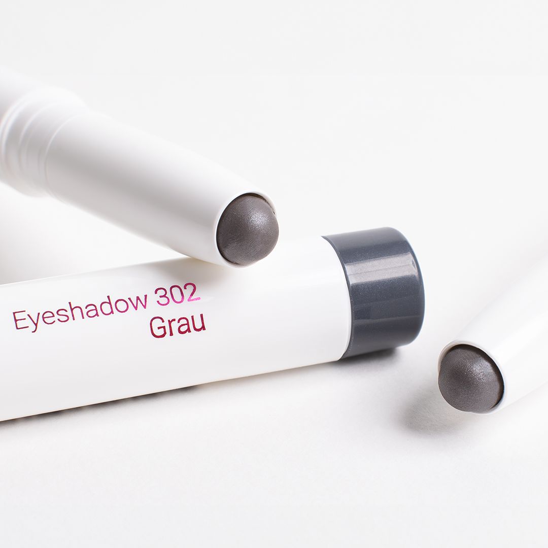 Drei graue Lidschattenstifte. Aufschrift: Eyeshadow 302 Grau. Weißer Stift, graue Spitze. Auf weißem Hintergrund.