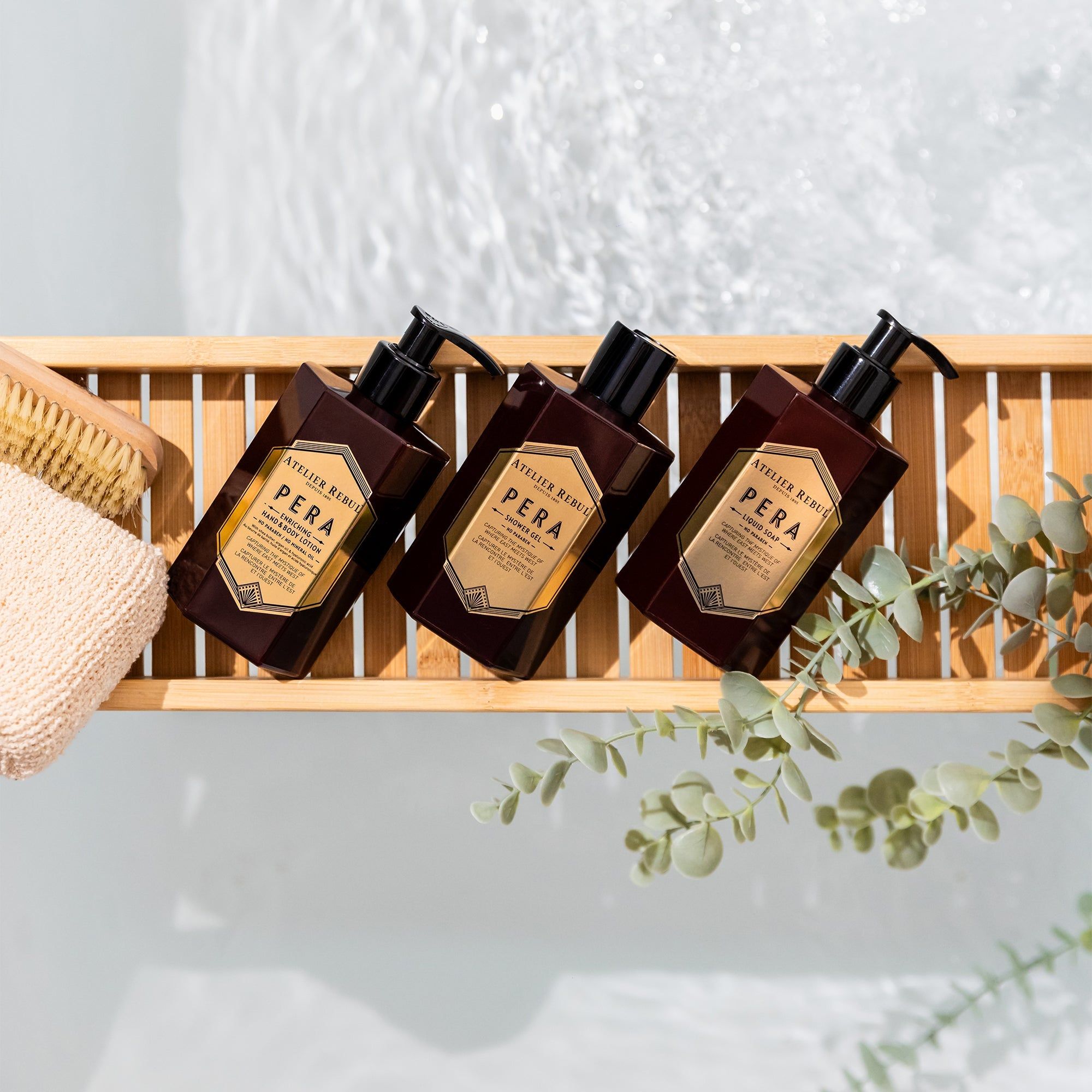 Drei Flaschen Atelier Rebul Pera Hand- und Körperlotion auf einem Holzgestell. Dunkelbraune Flaschen mit schwarzen Pumpköpfen. Goldfarbene Etiketten.